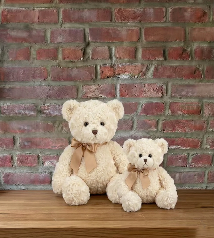 Two teddy bears with ribbons sitting on a wooden surface against a brick wall.